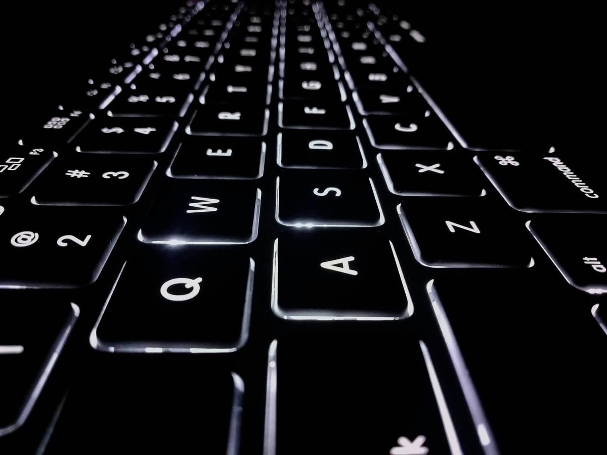 Close-up of an illuminated keyboard in a dark setting, showing keys from angle, with letters and symbols visible.