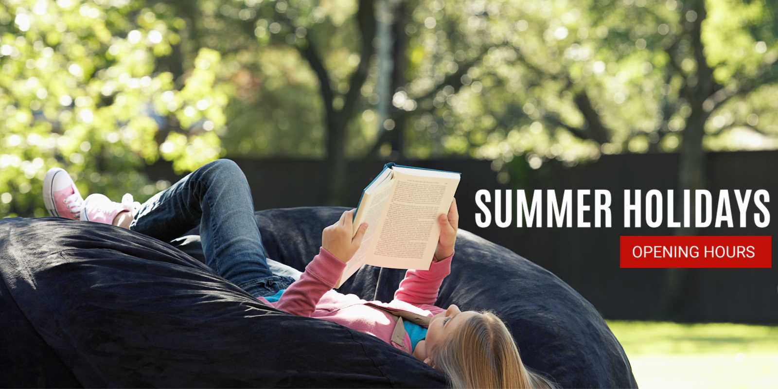 Student reading a book on a beanbag outside on the grass. She looks very comfy.