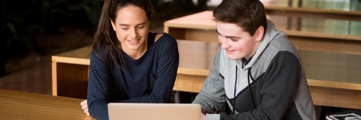 Two students sitting in front of an open laptop