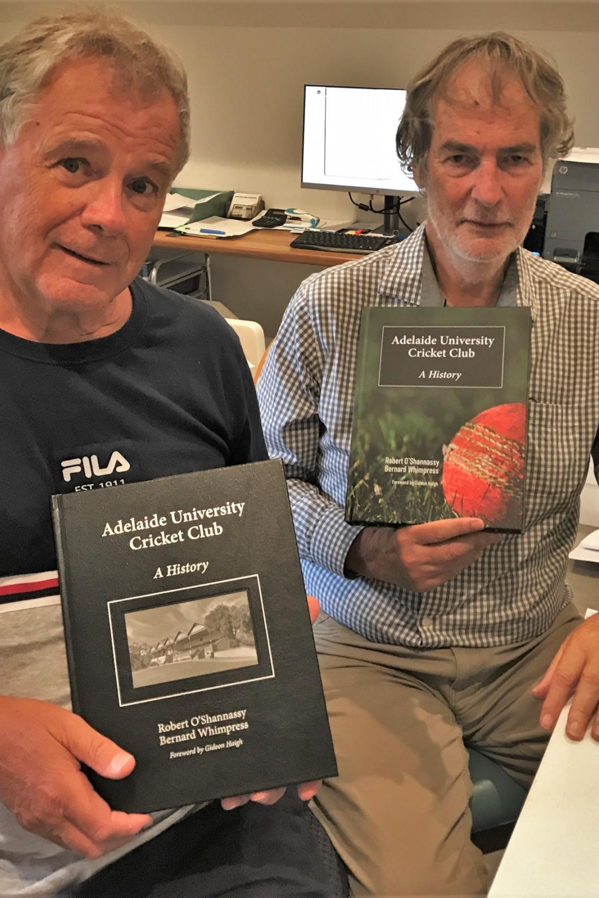 Authors, Robert O'Shannassy and Bernard Whimpress sitting next to each other and holding up books about the cricket club