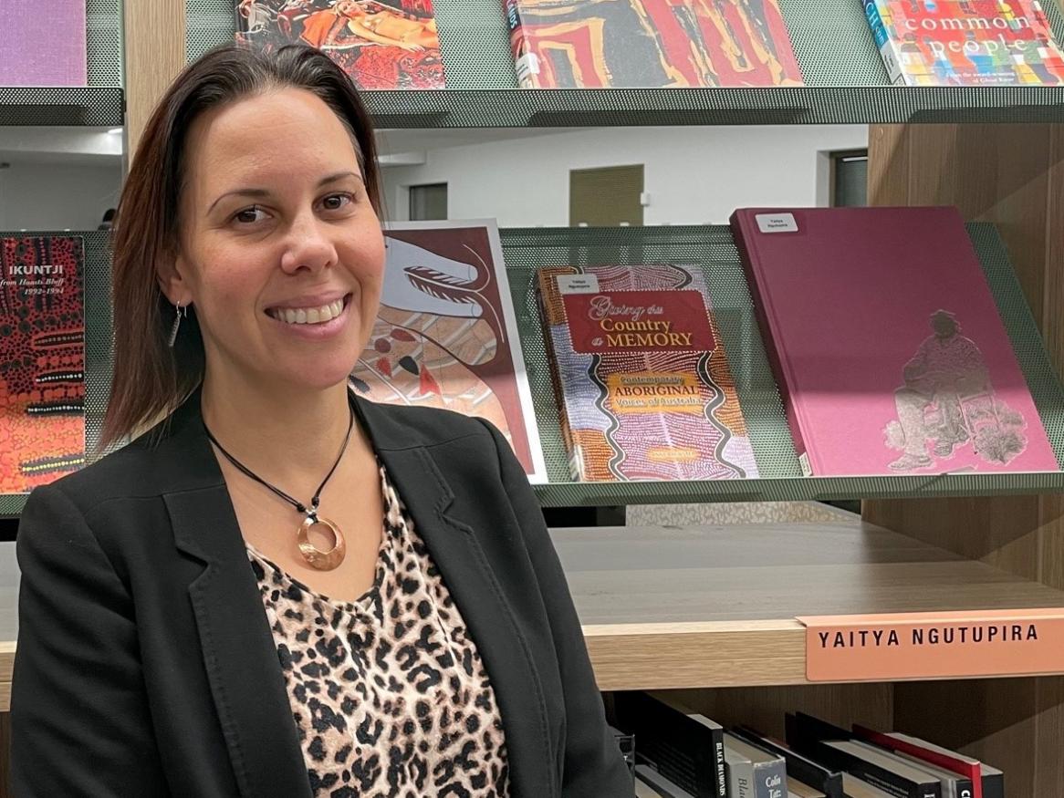 Photo shows Renee Johnson, Indigenous Librarian, in front of a shelf of books from the Yaitya Ngutupira collection