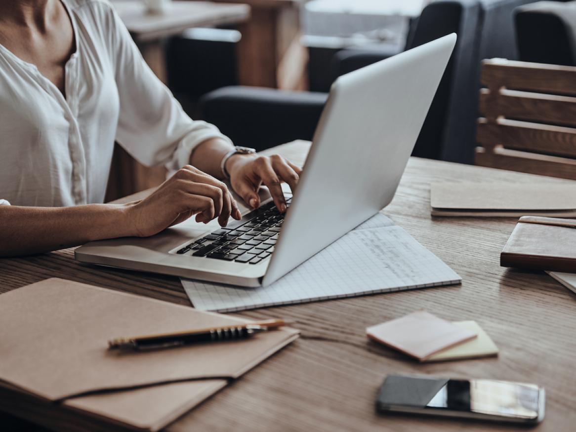 Woman using a laptop on a desk surrounded by papers