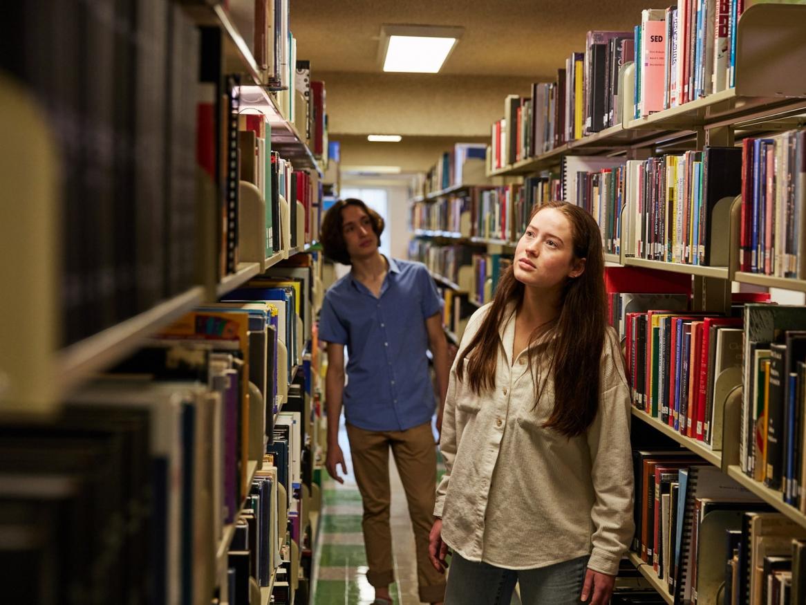 Two students browsing books on the shelves of the library