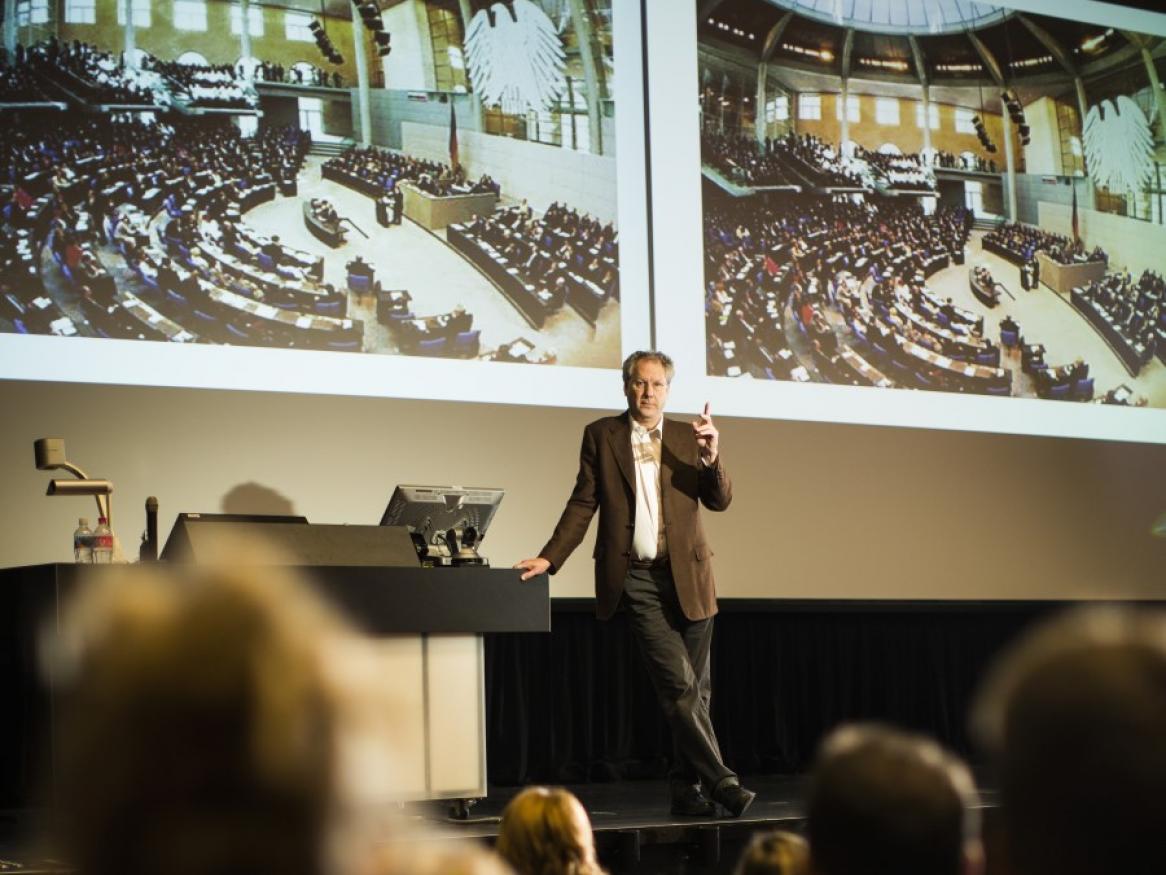 Lecturer standing on stage with two big screens behind him