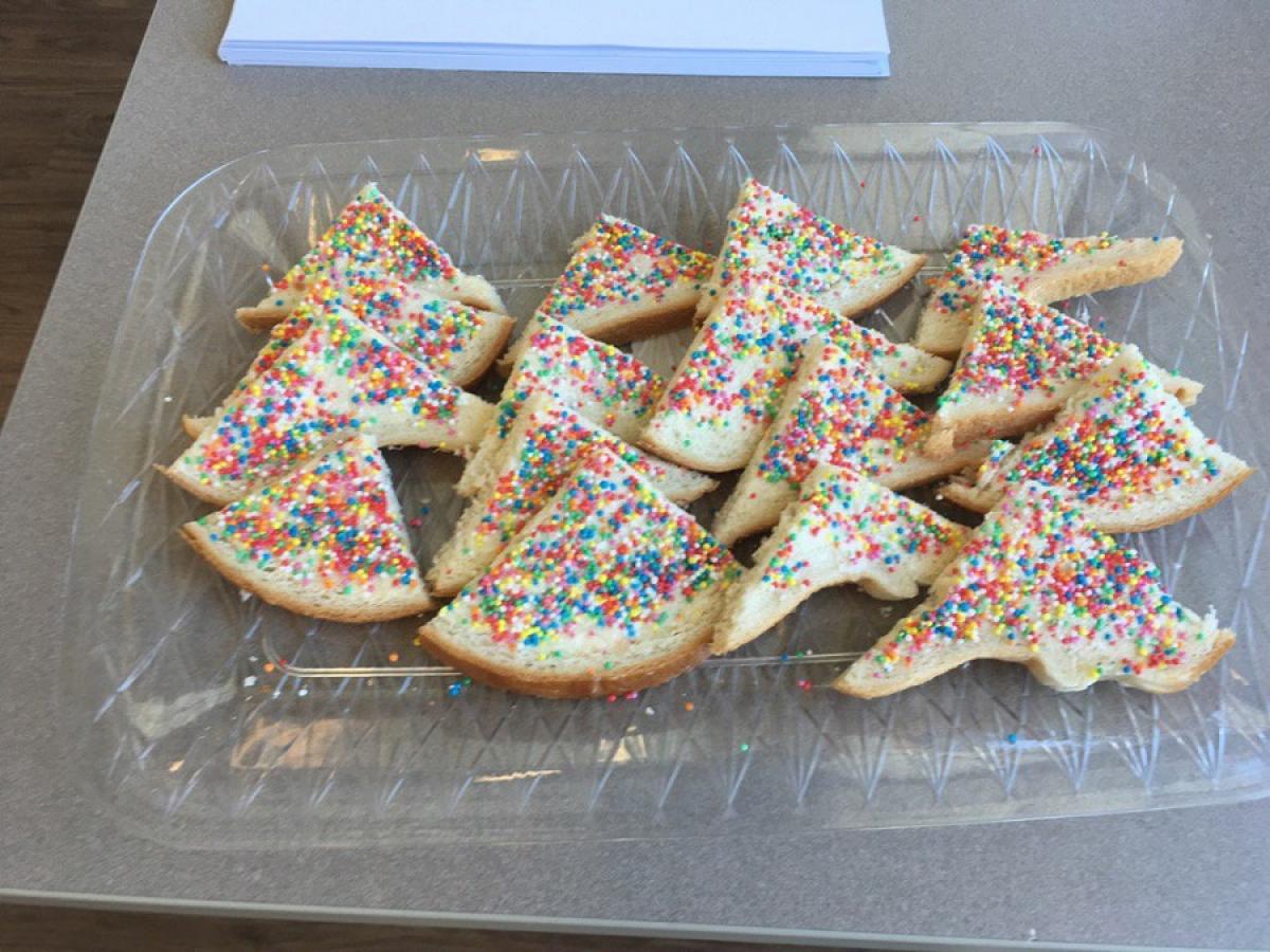 A tray of fairy bread triangles. That is, bread spread with butter and with hundreds and thousands (tiny ball shaped coloured sprinkles) sprinkled on top.