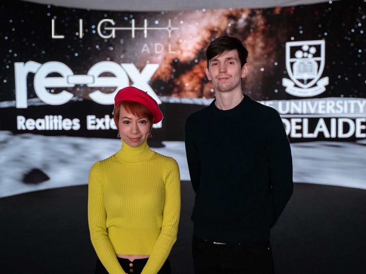 Annie and Matthew stand and smile in front of the innovative Light Adelaide screens.