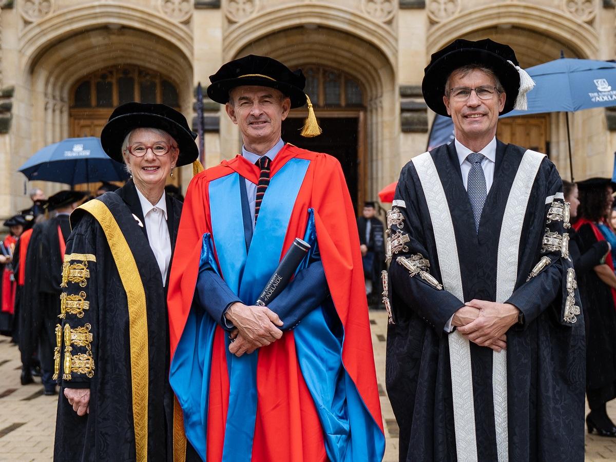 Mr Ian Alexander Scobie AM smiles and holds his honorary doctorate, with the Hon. Catherine Branson AC KC and Vice-Chancellor and President, Professor Peter Høj AC.