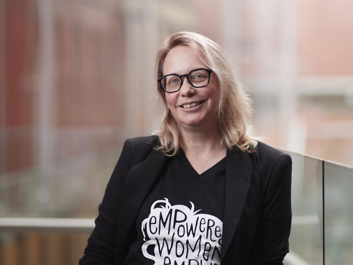 Professor Katrina Falkner smiles into the camera, wearing a shirt that says 'Empowered women empower women'.