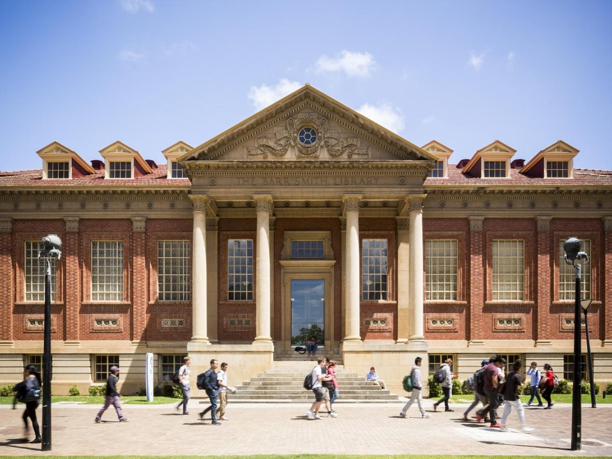 Students walk around the Barr Smith Library, with a blue sky above.