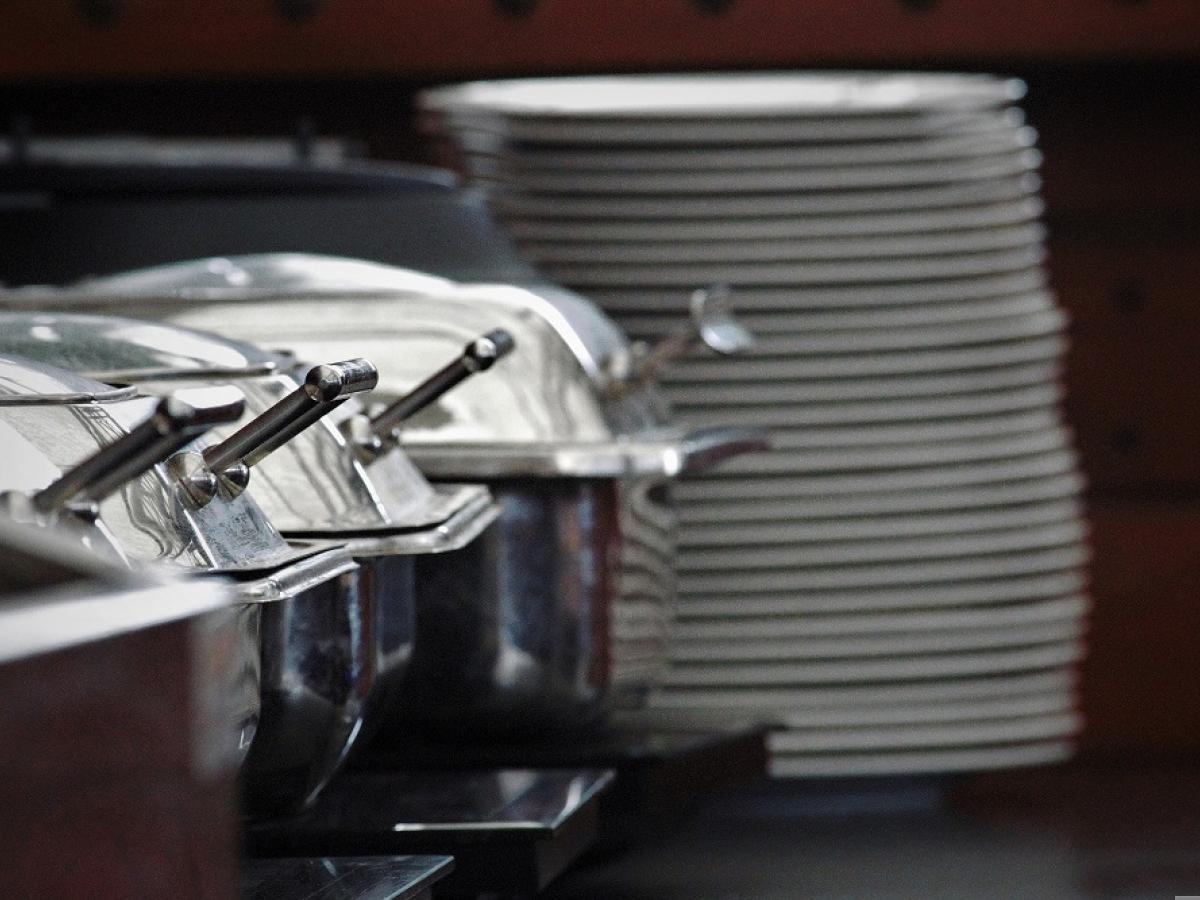 A buffet with silver food warmers and a stack of plates.