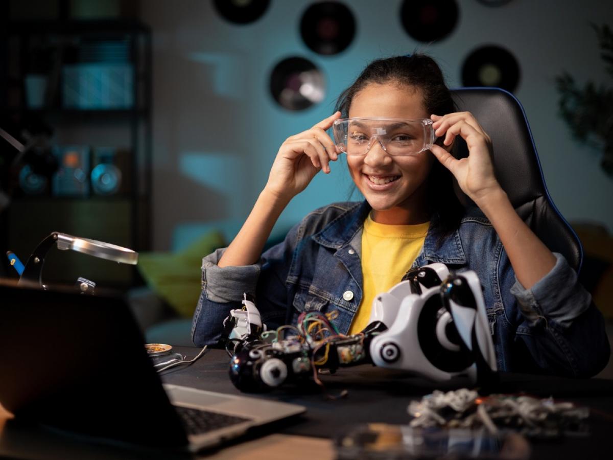 A girl smiles while working with a robot and computer.