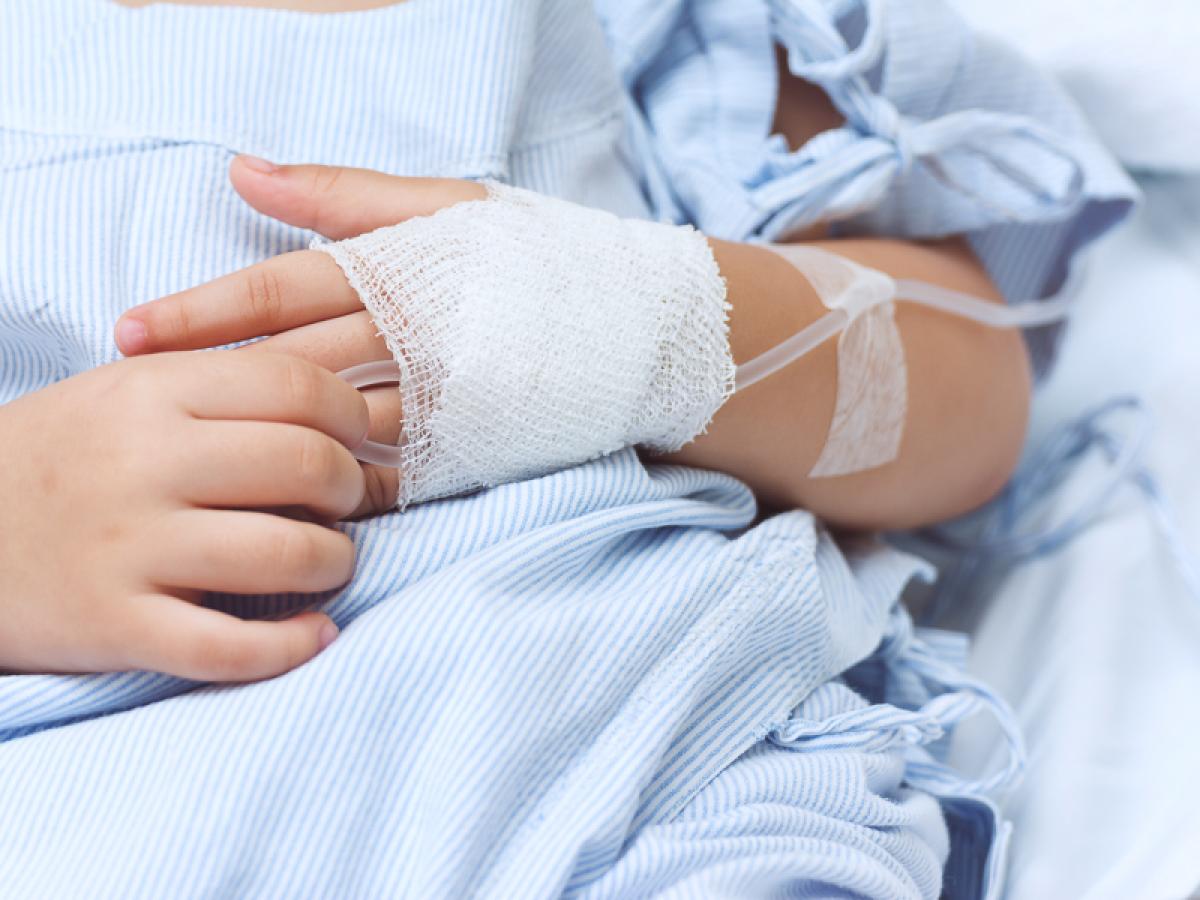 A child in a hospital bed with a drip in their hand.
