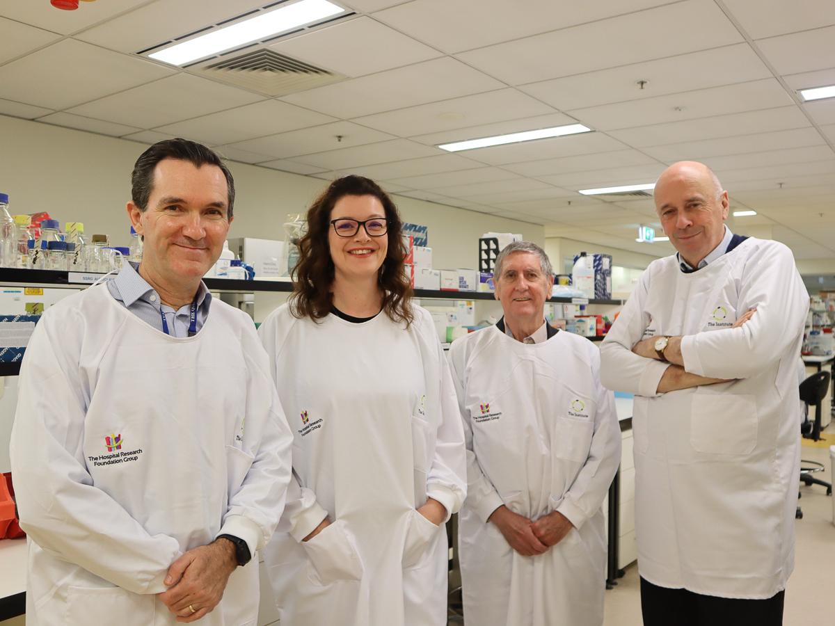 A group of four people stand in white coats in a medical laboratory.