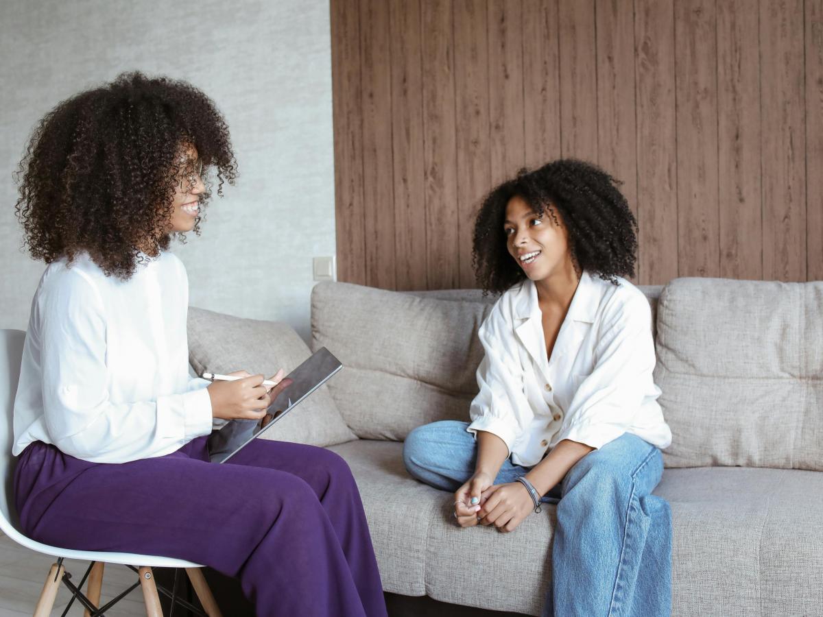 Two women sit on a couch and a chair.