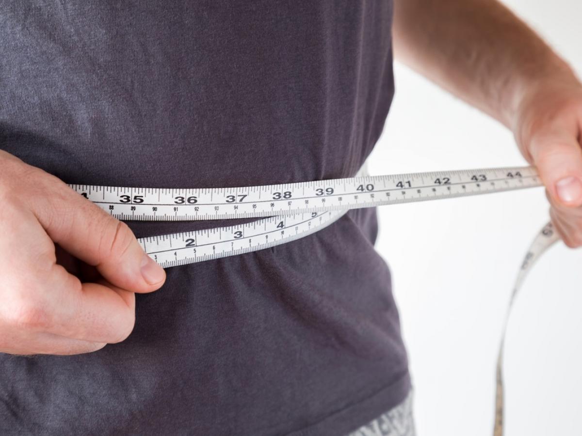 Stock image of man's waist. He is holding a tape measure around his waist.