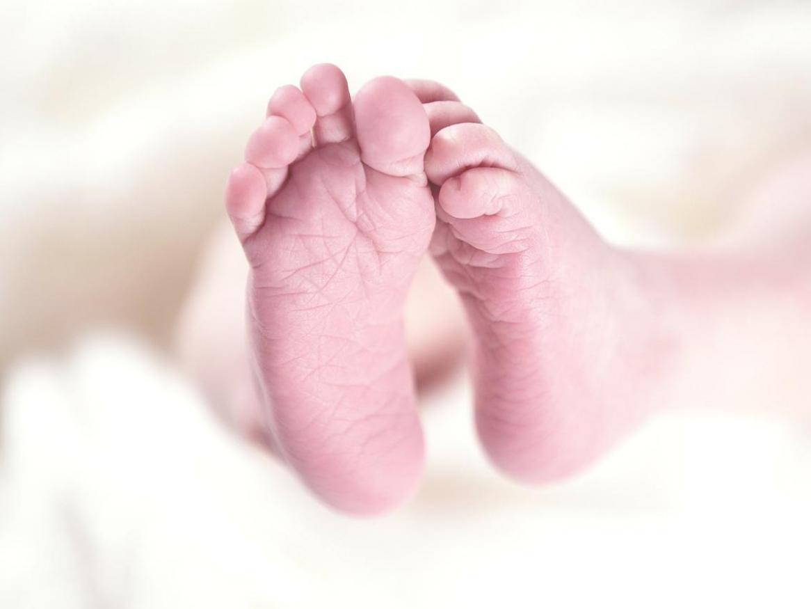 The feet of a baby poke out from underneath a blanket.