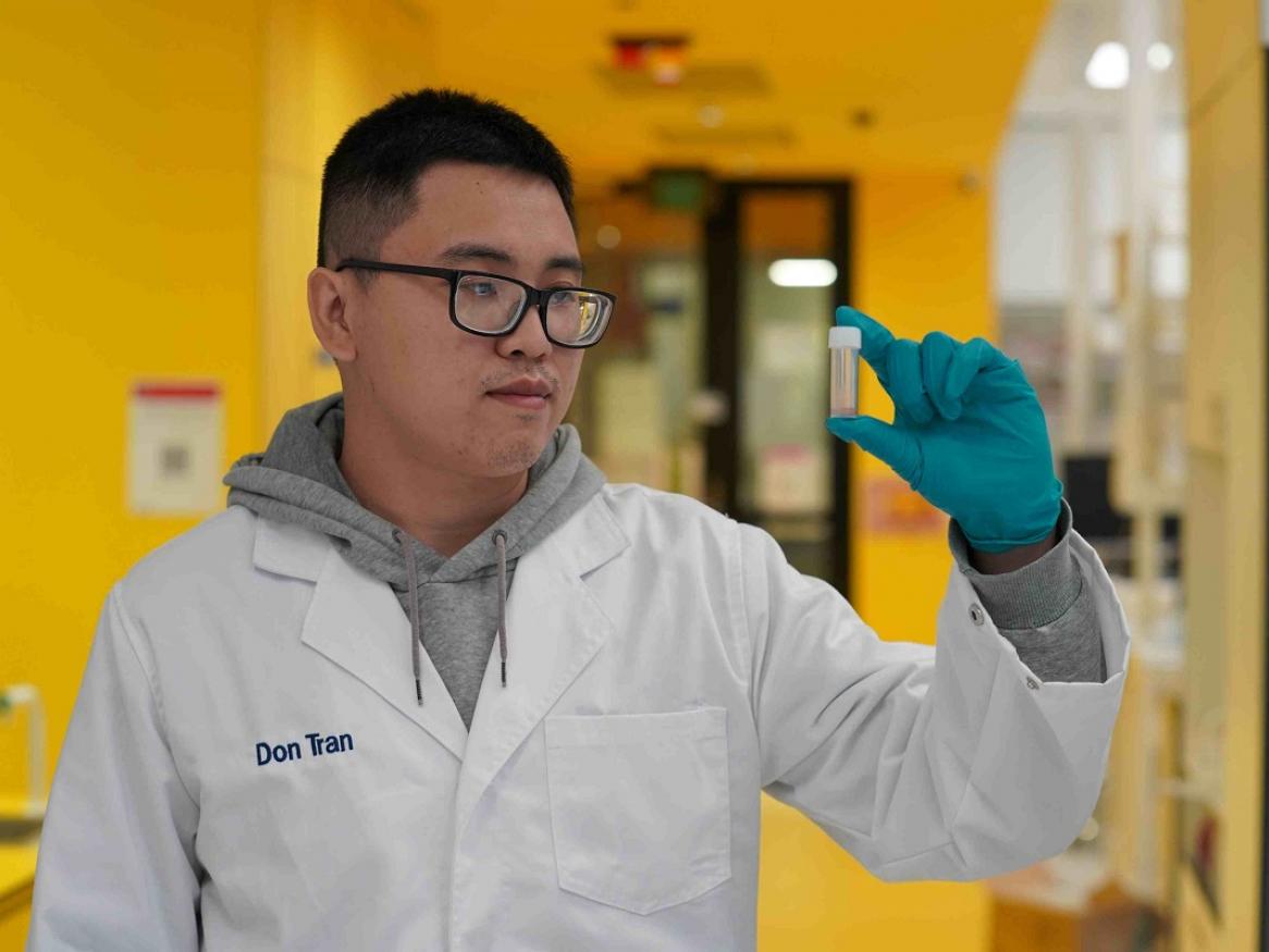 Don Tran stands, holding a sample of the tablets that had been to space.