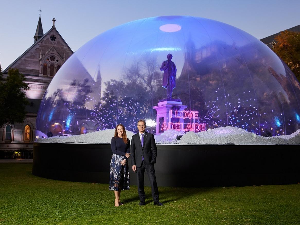 Jess Gallagher and Peter Hoj stand, smiling, in front of the snowglobe installation at the University of Adelaide.
