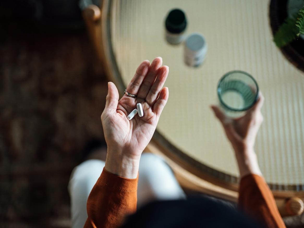 A person holds a glass of water and tablets.