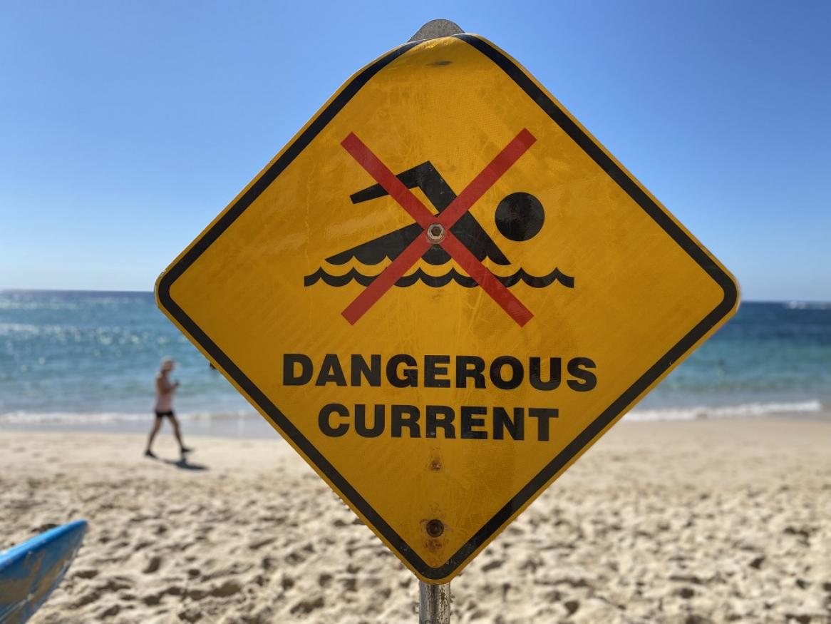 A yellow sign on a beach read "DANGEROUS CURRENT"