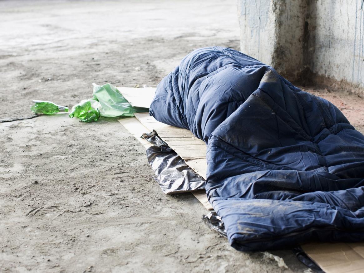 A homeless person lies on the ground in a sleeping bag.