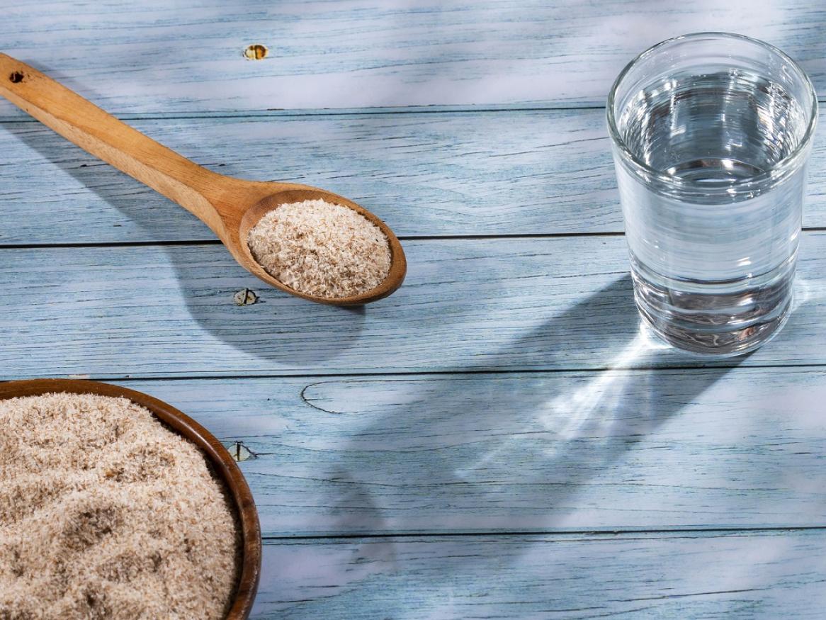 A spoon with psyllium powder, a bowl containing psyllium and a glass of water