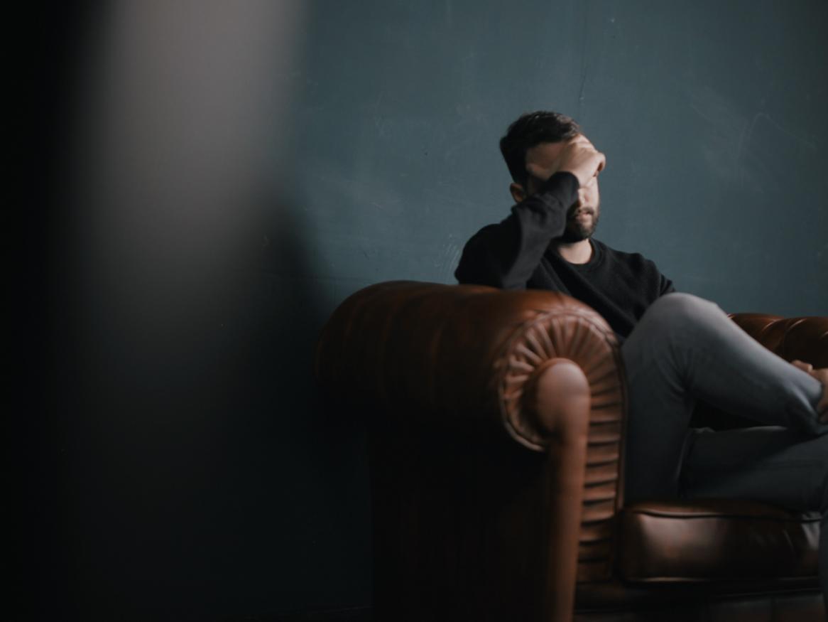 Man sitting on a chesterfield lounge with his head in his hands.