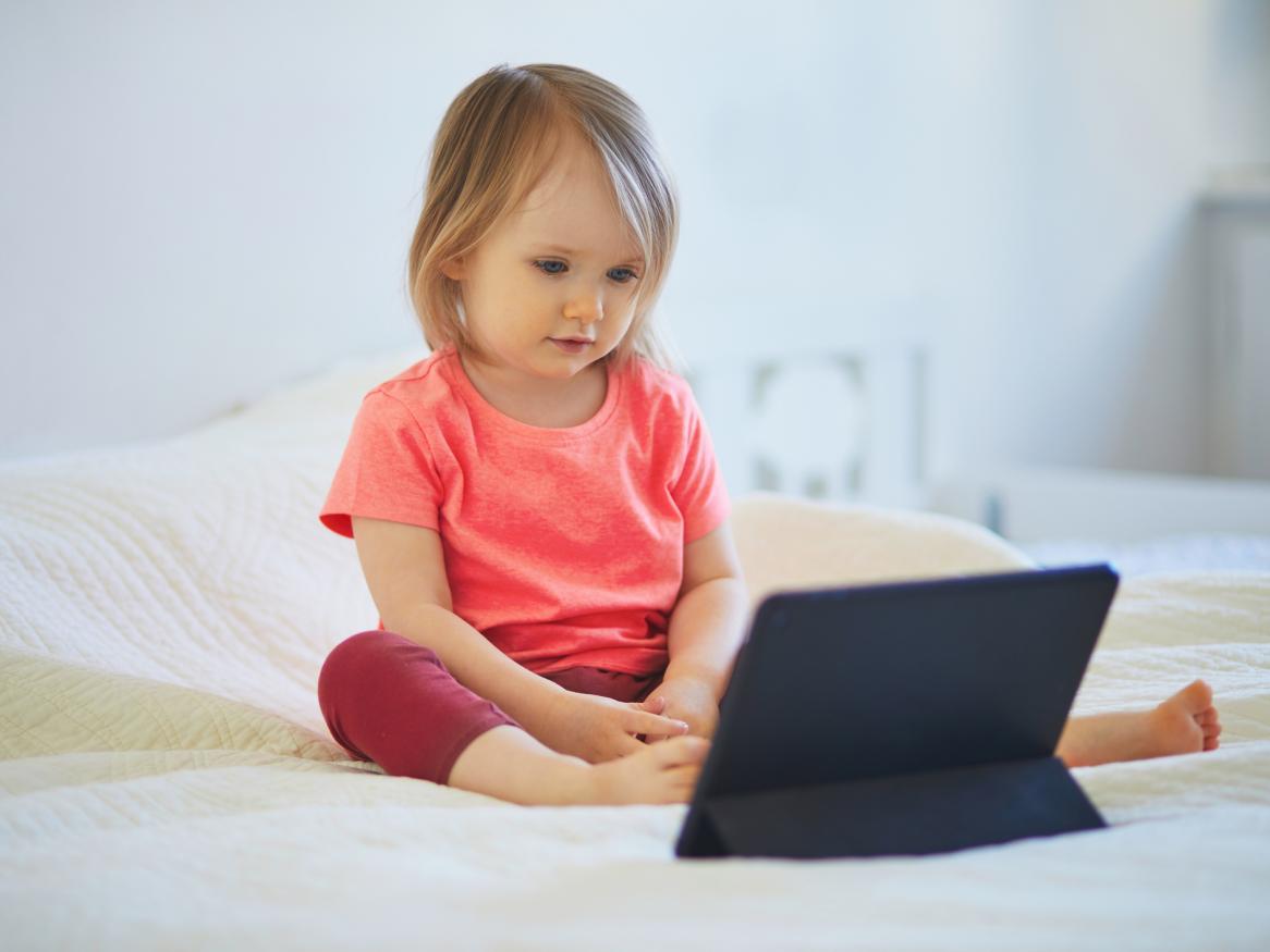 Toddler sitting in front of a digital tablet. She is watching the screen.