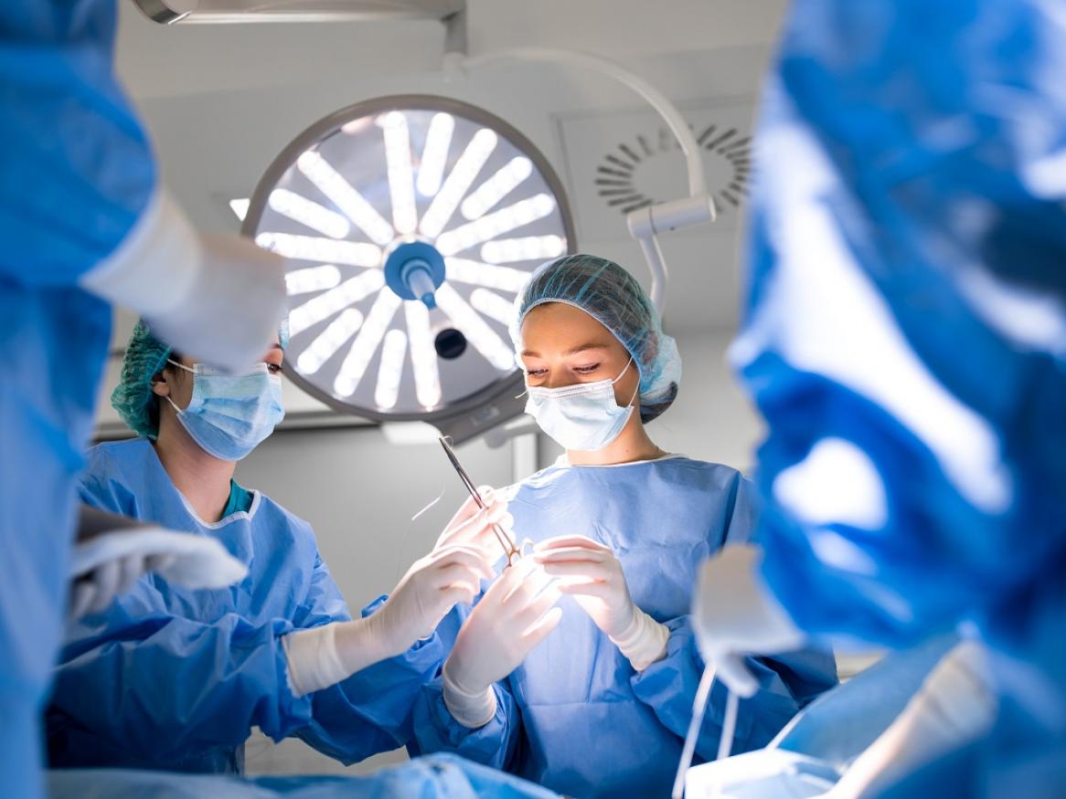 Stock image of surgeons in an operating theatre. One surgeon is being passed a pair of scissors.