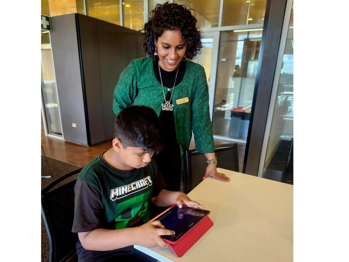 Dr Abi Thirumanickam standing next to a study participant who is playing minecraft on an ipad.