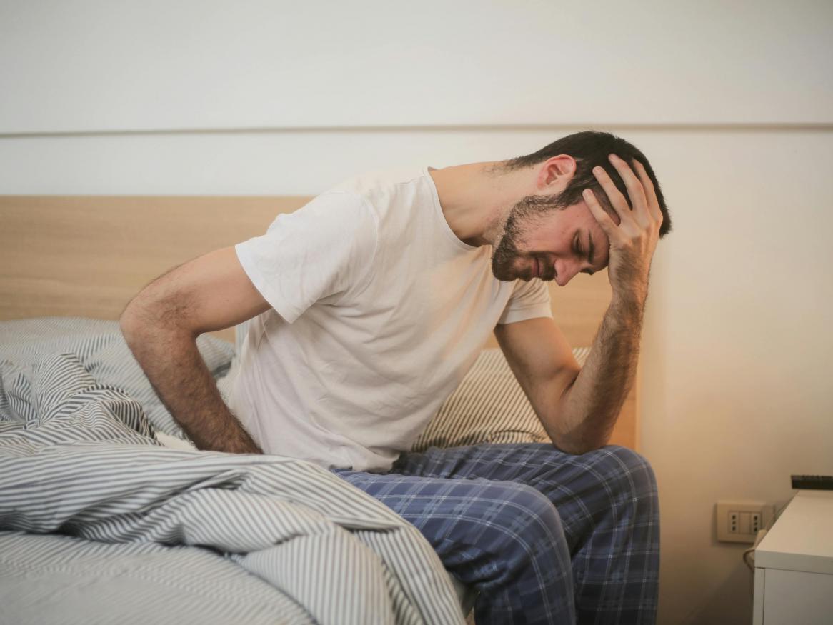 A man sits on a bed with his head in his hand.