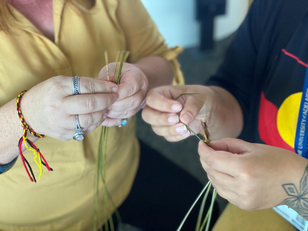 Two sets of hands are holding materials for weaving.