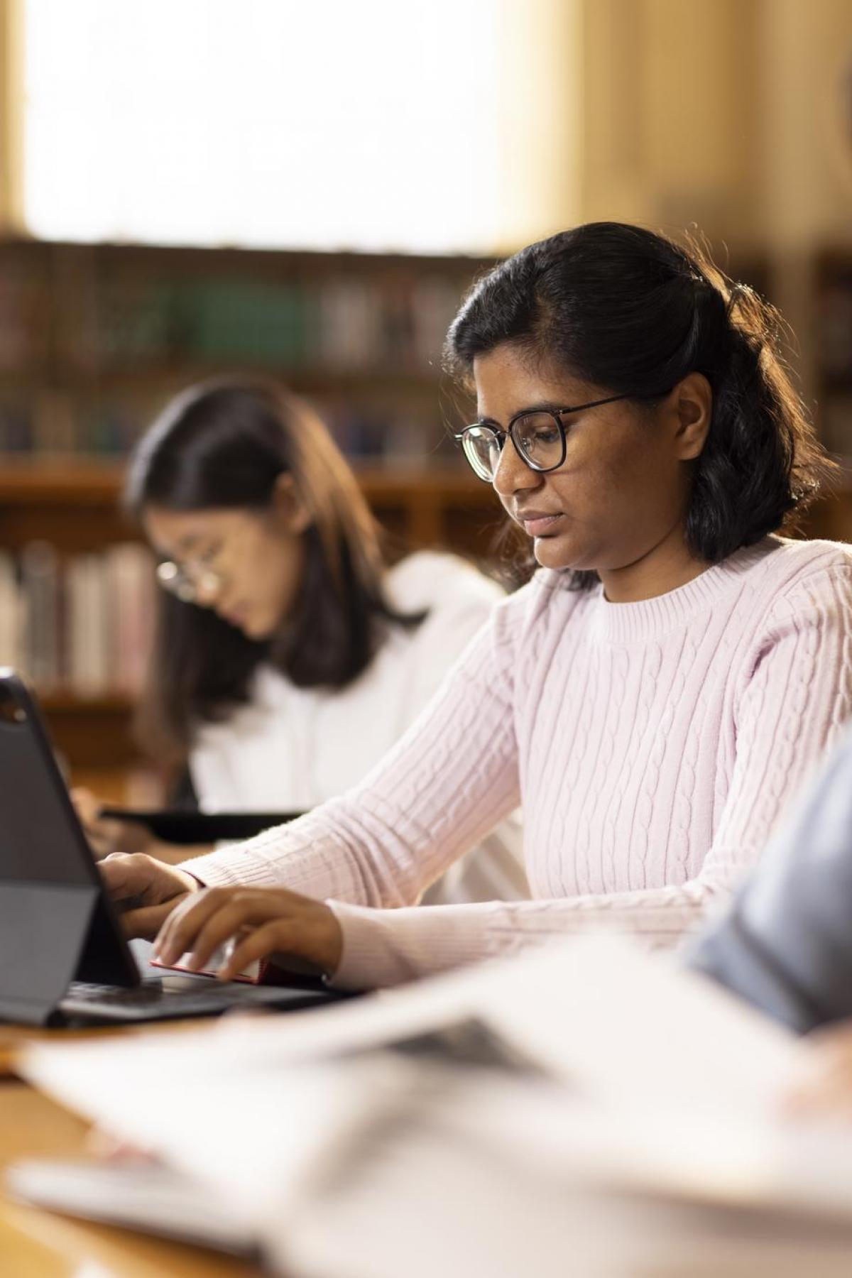 Student wearing knitted jumper and glasses studying on laptop