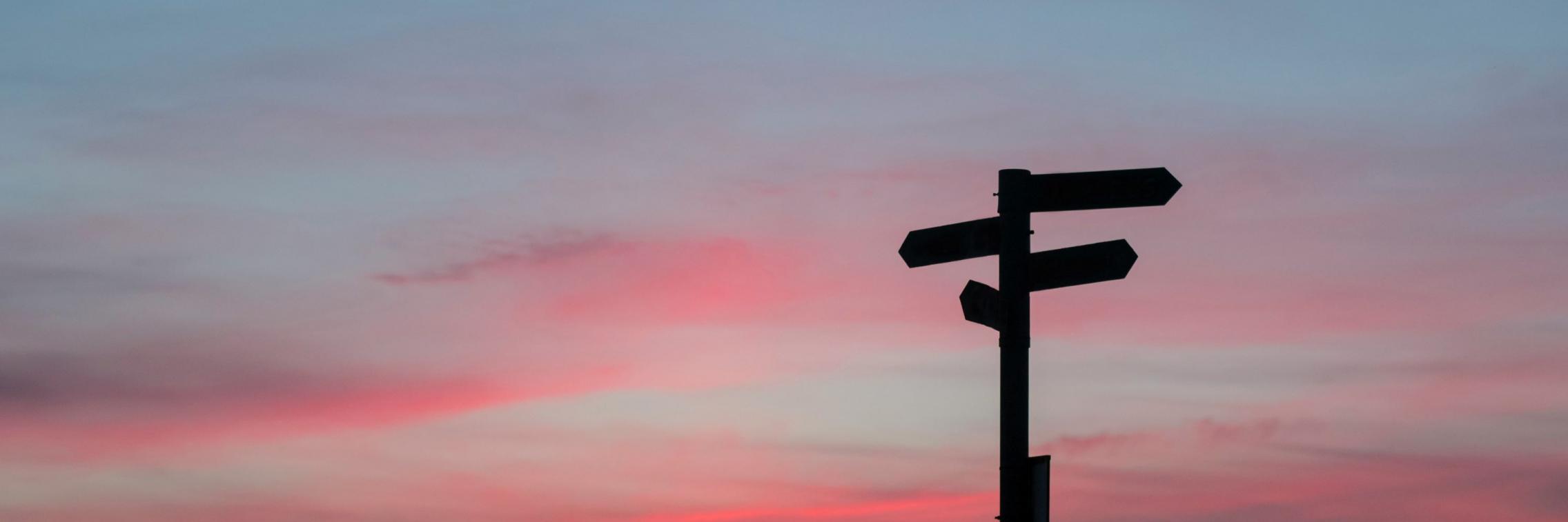 A silhouette of a street sign with arrows pointing in multiple directions at sunset.
