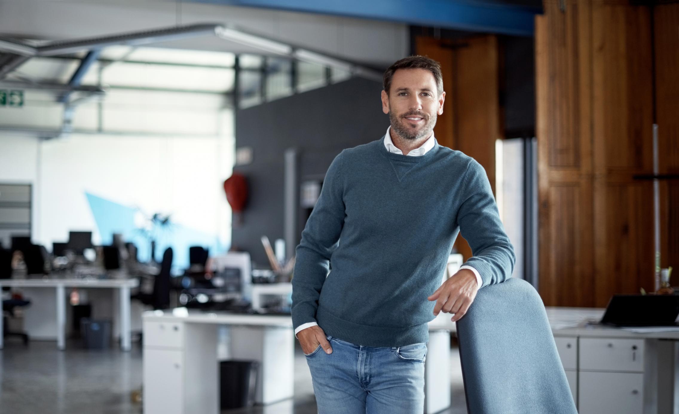 Male standing, leaning on a chair, smiling