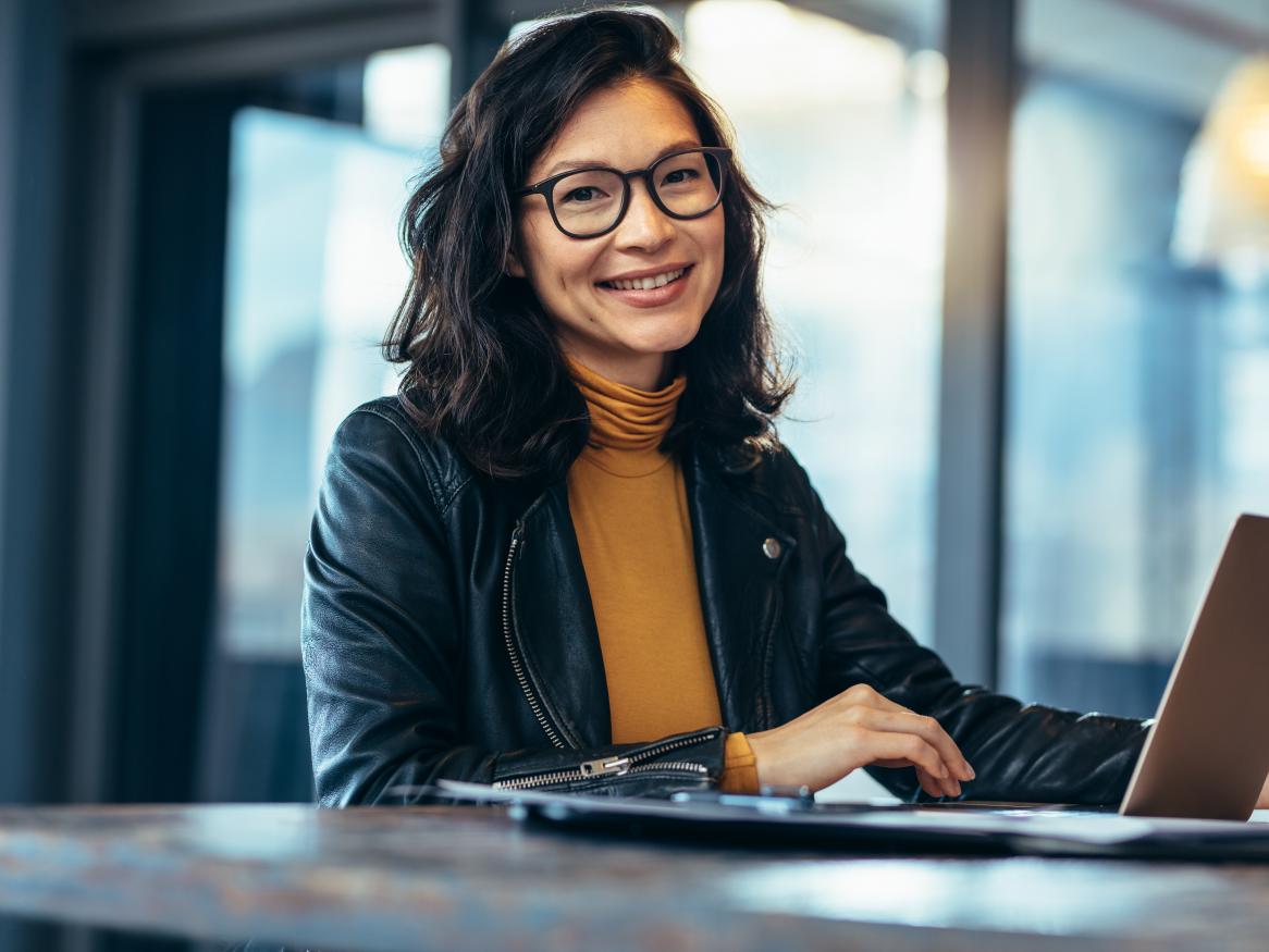 Portrait of attractive business woman sitting at her desk with laptop computer in office. Smiling business woman in casuals at office.