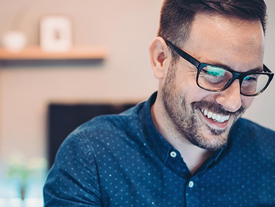 Male looking down and at a laptop and smiling