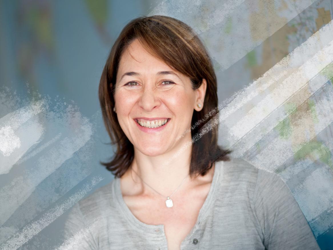 Smiling female holding a textbook with a world map in hte background.