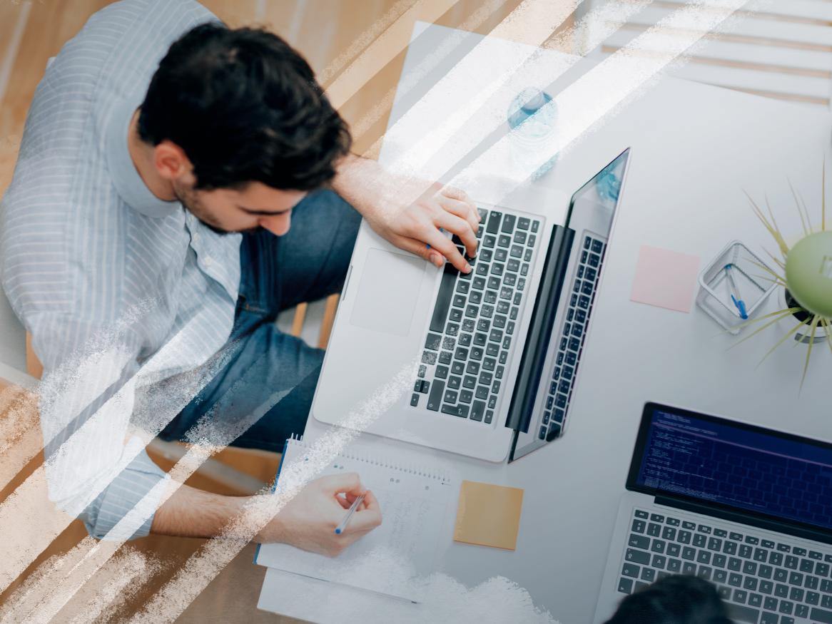 Aerial view of male sitting at a desk with laptop, pen and paper