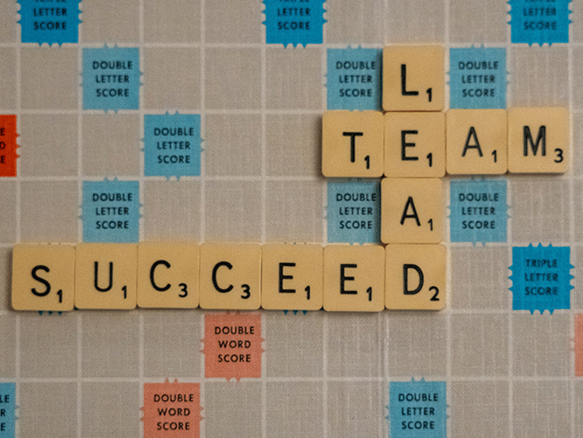 Scrabble board with the words 'lead, team, and succeed' spelled out on scrabble tiles