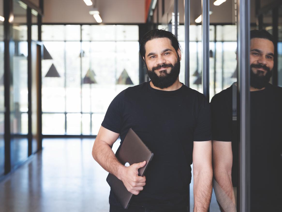 Man standing in corridor holding laptop.