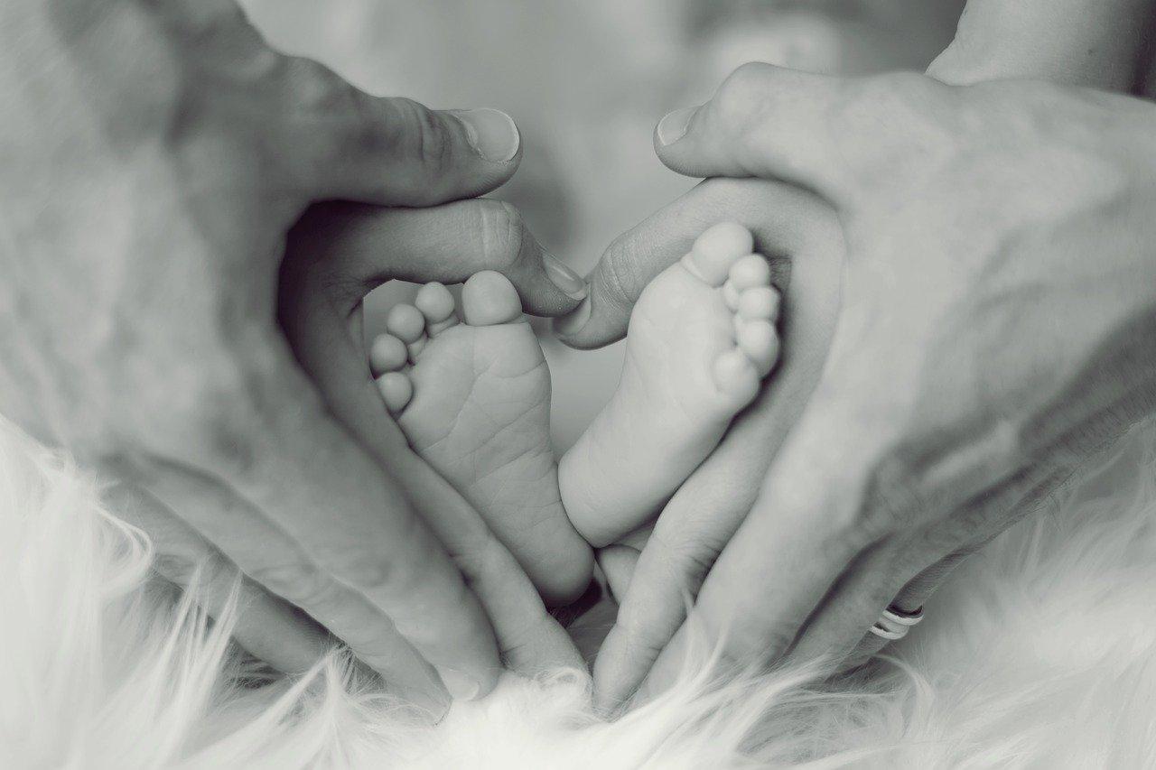 Baby feet held by hands of two adults