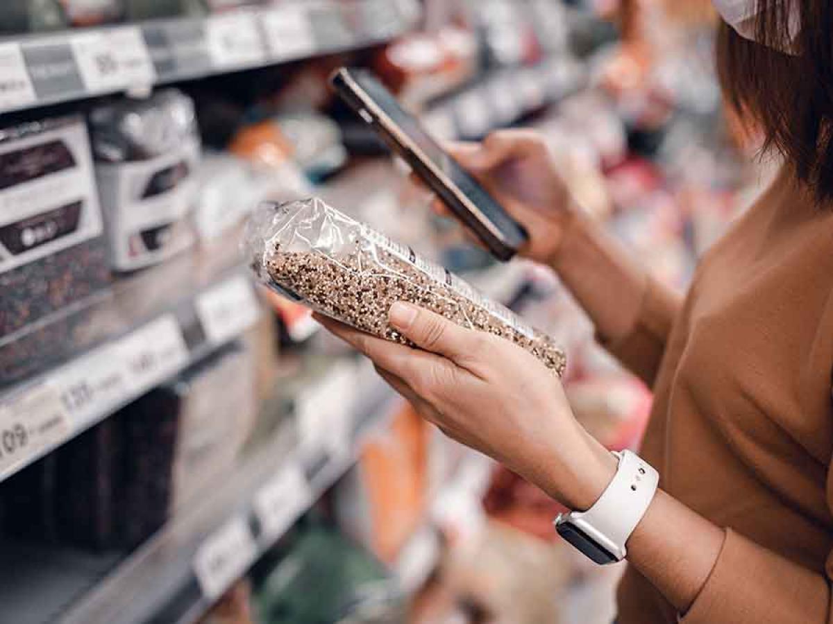 A woman in a grocery isle looking at nutritional guidelines and her phone