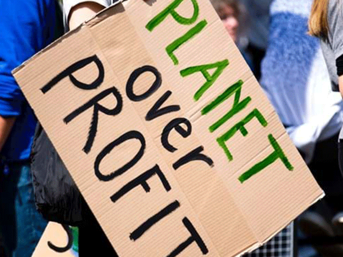 Crowd at a demonstration holding a sign that says Planet over Profit