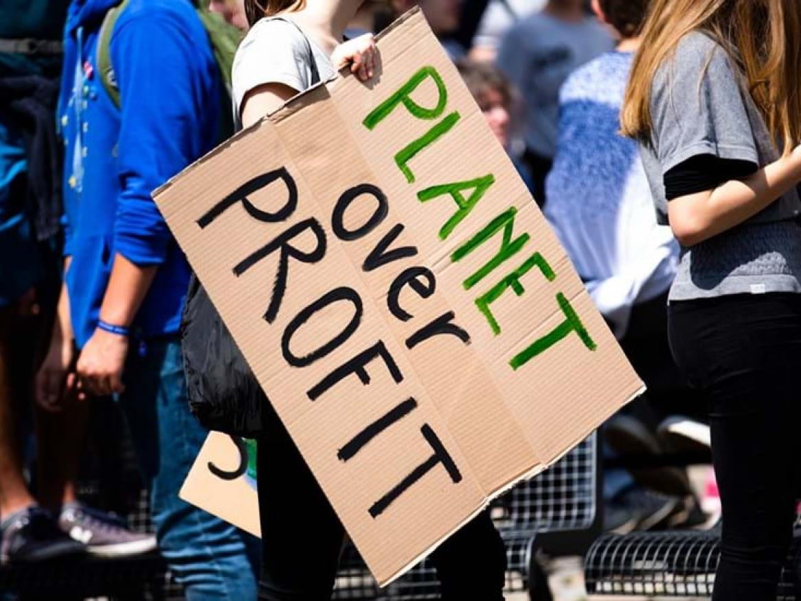 Crowd at a demonstration holding a sign that says Planet over Profit