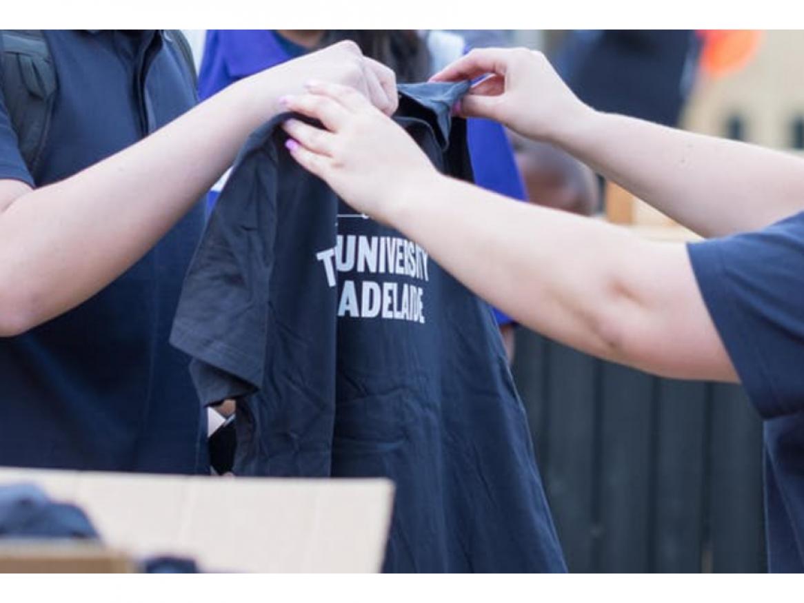 One person handing a University of Adelaide shirt to someone else