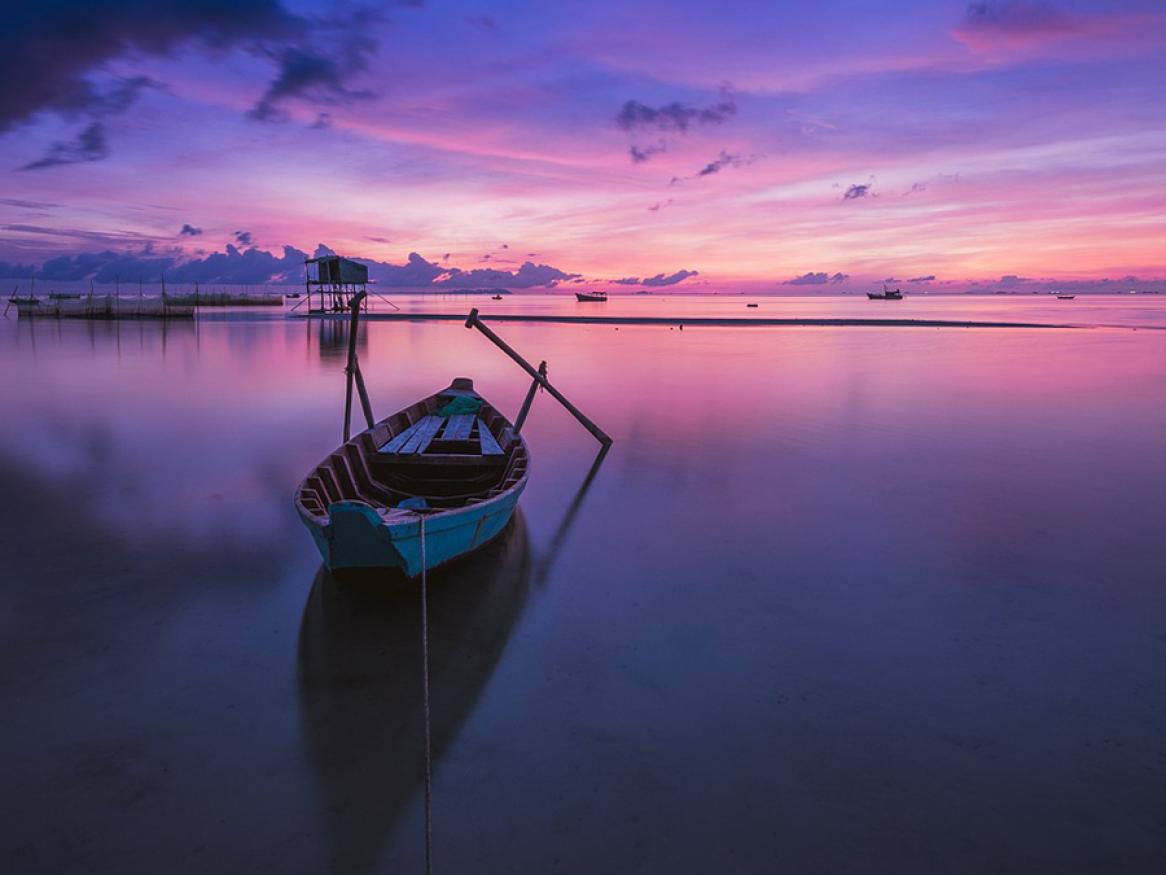 Purple and pink sunrise over water in vietnam with small boat in forground