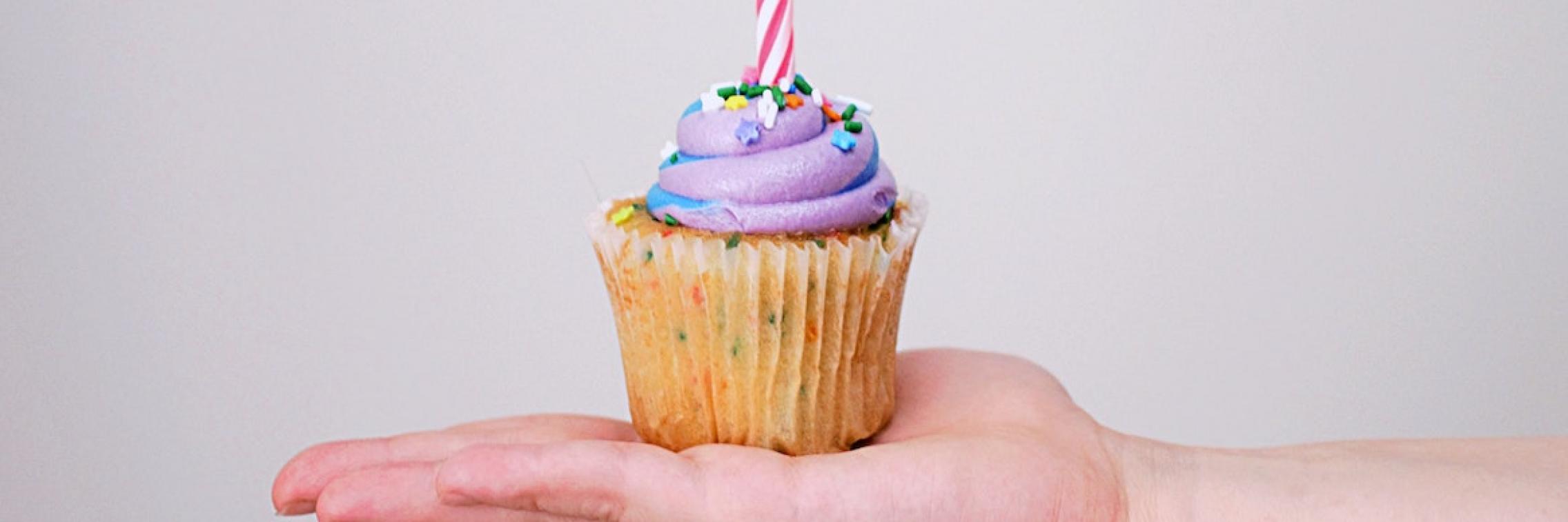 A person holding a birthday cupcake.