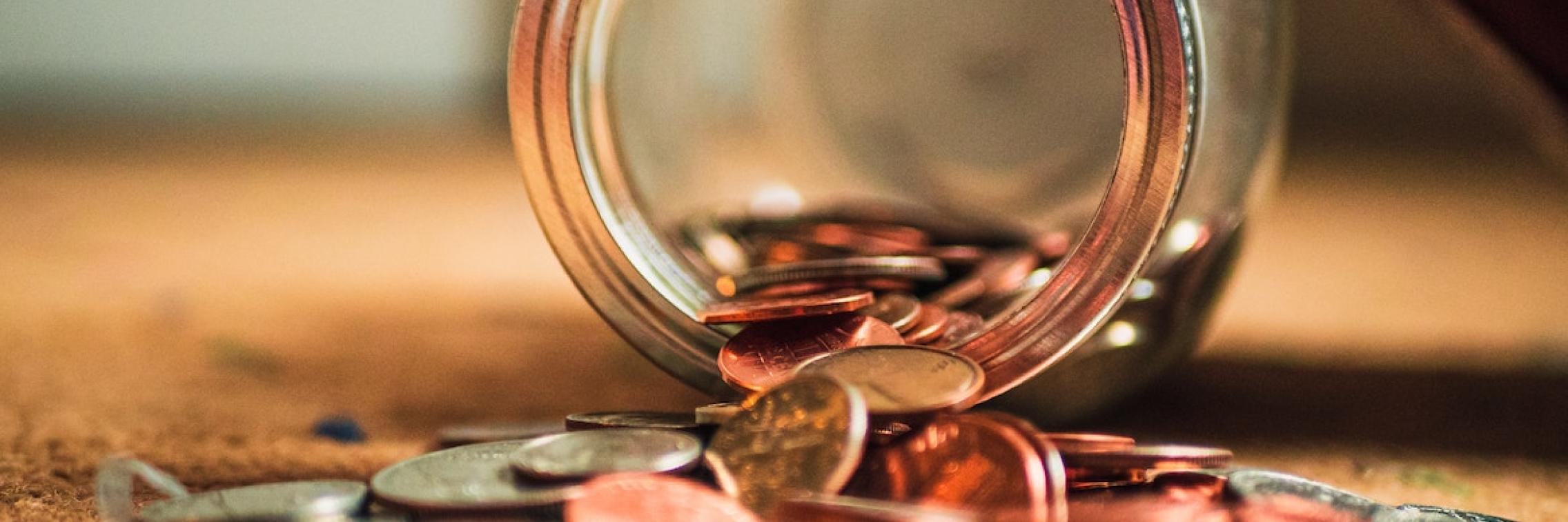 Coins spilling out of a glass jar.