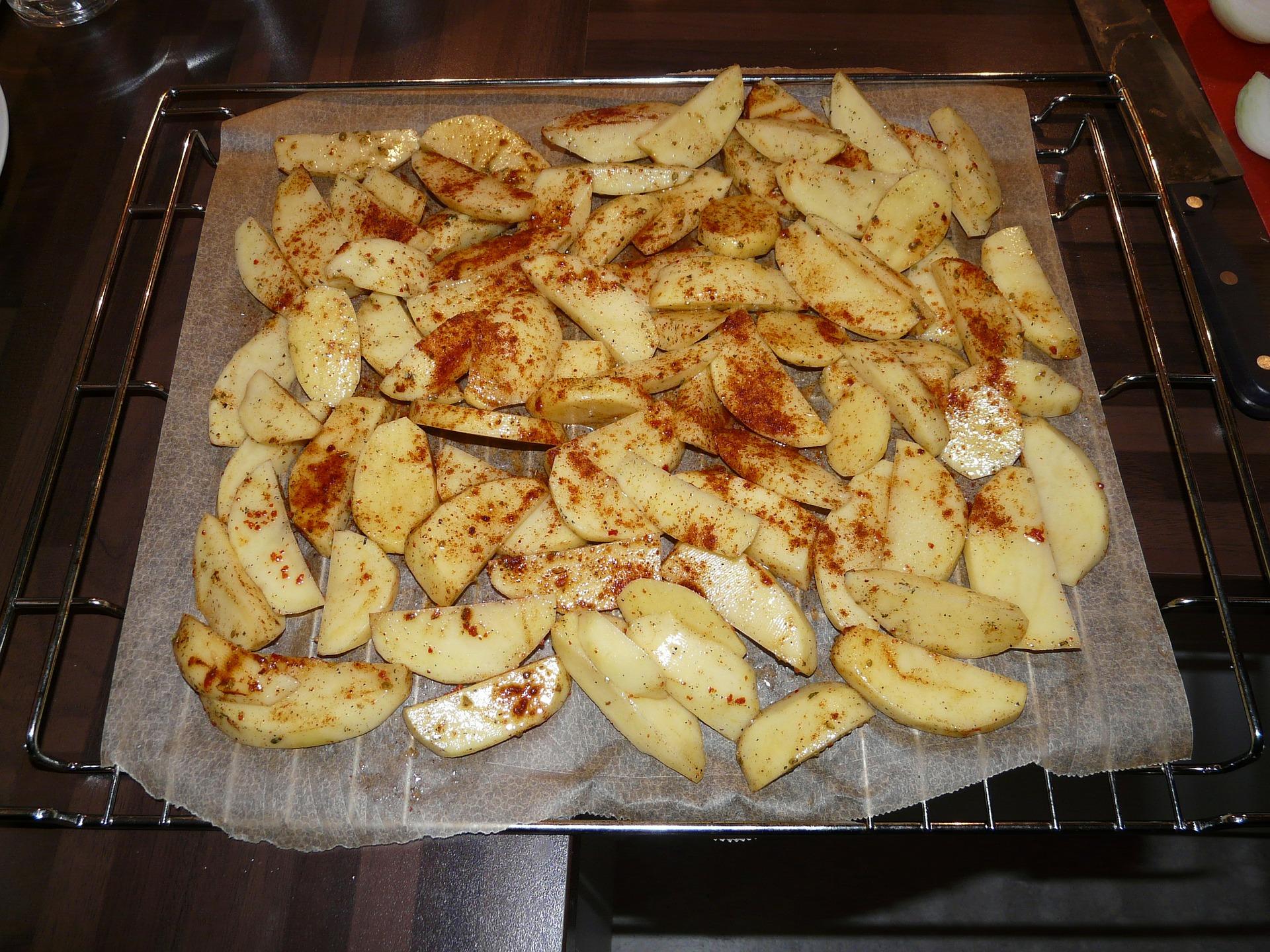 Raw potato wedges with paprika on an oven tray.